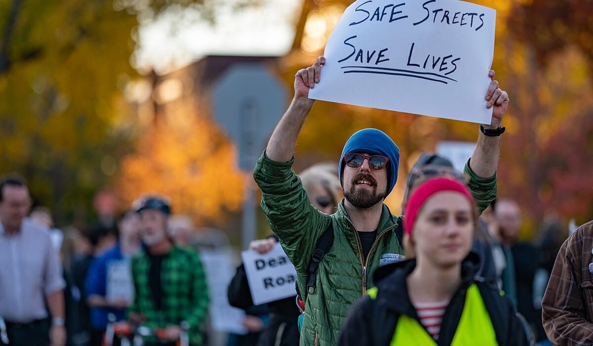 A protester holds a sign that says "Safe Streets Save Lives"